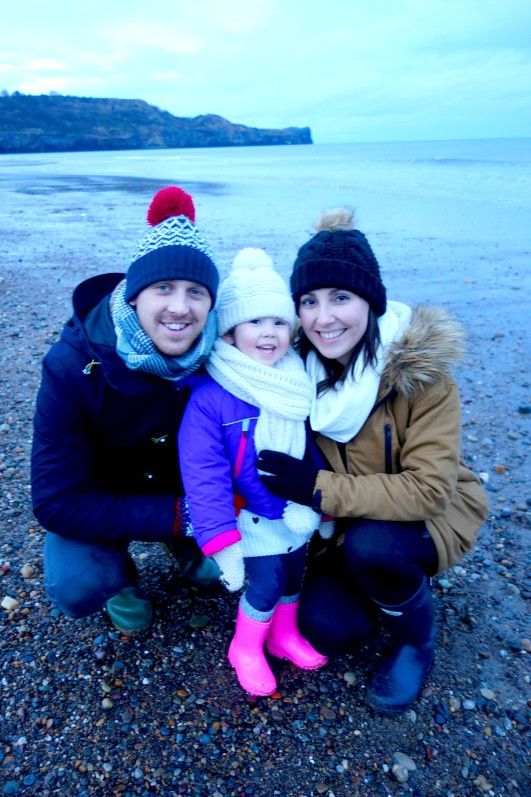 mum, dad, and daughter crouching together and smiling on beach