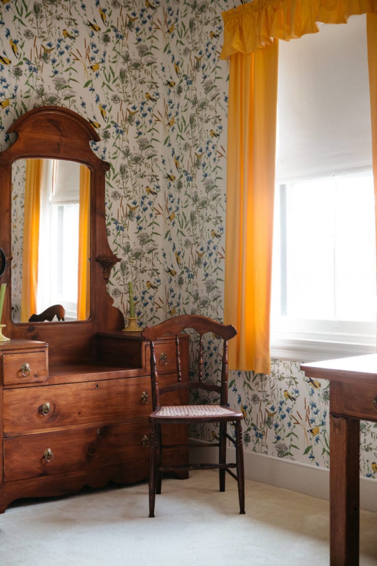 bedroom with wooden dressing table with mirror and yellow curtains at the window