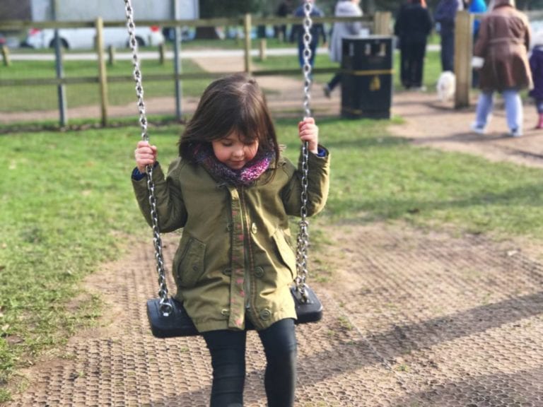 young girl in coat and scarf on swing