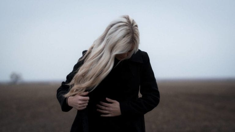 woman with long blonde hair outside, holding her belly