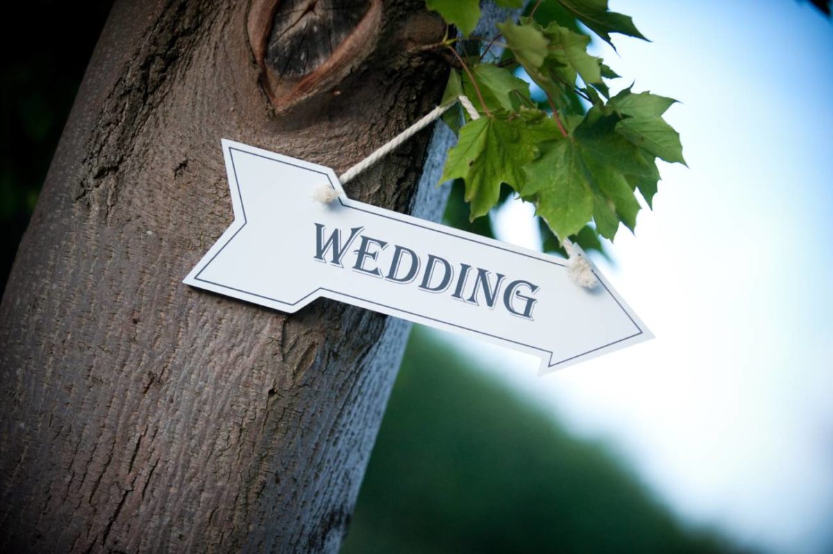 white wooden wedding sign shaped as an arrow hanging on a tree