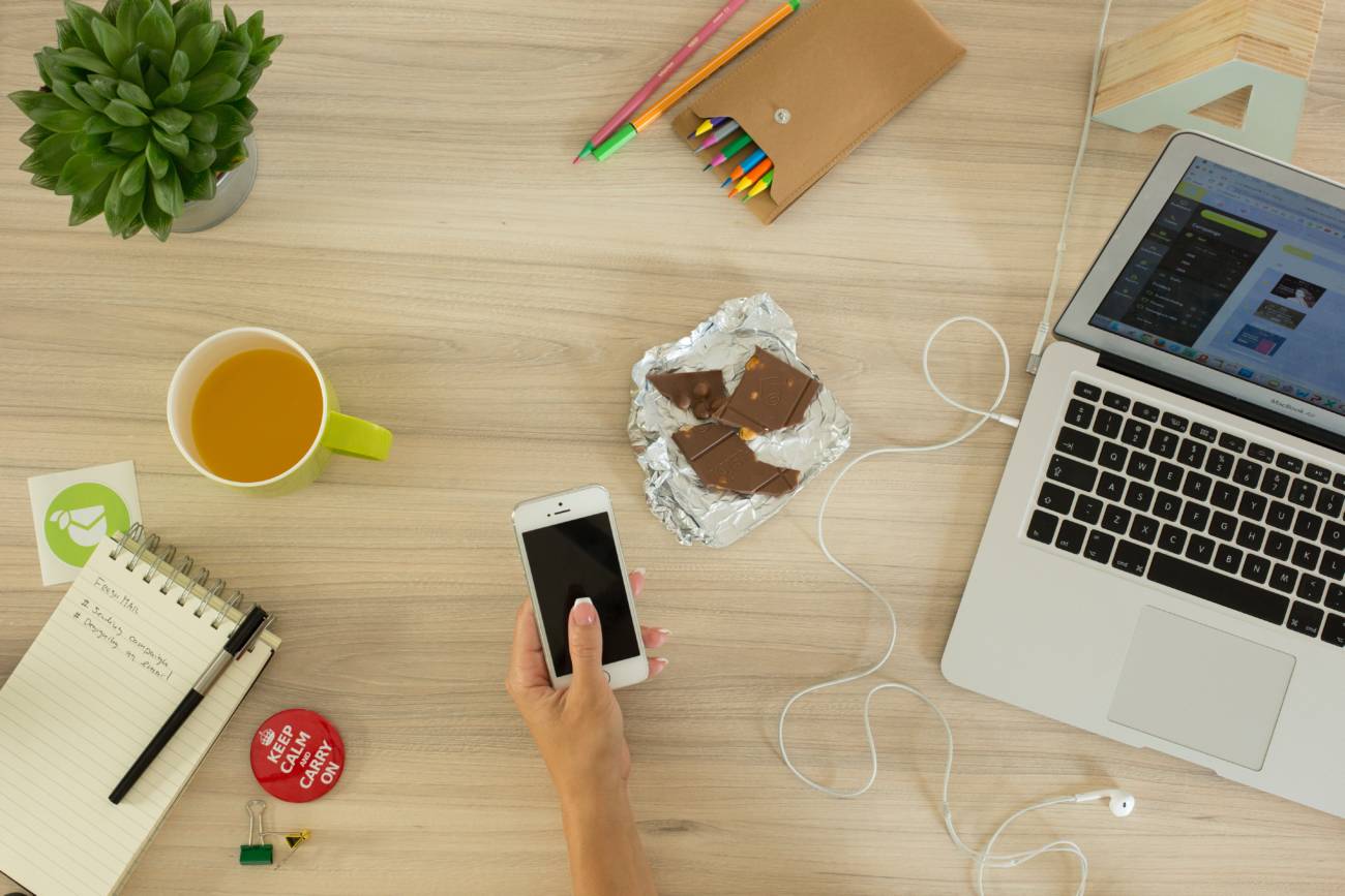 desk from above with phone, laptop, pens and chocolate