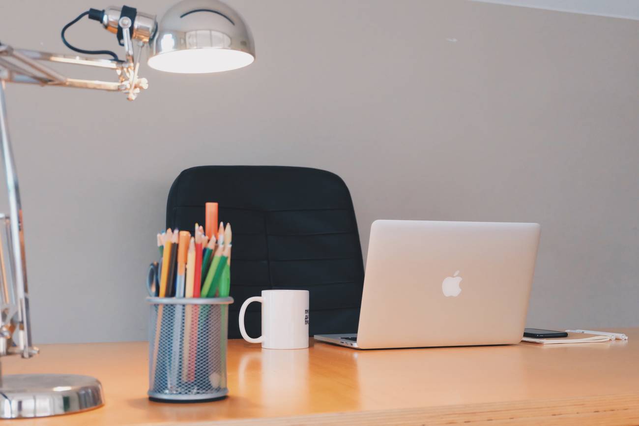 desk with open laptop on it and pen pot of pens, mug and chair pushed under it