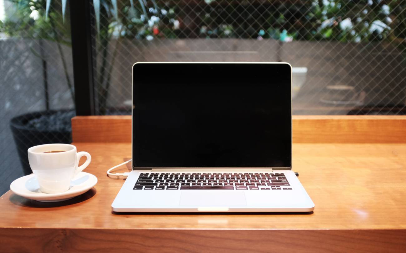 open laptop on table in coffee shop with cup and saucer next to it