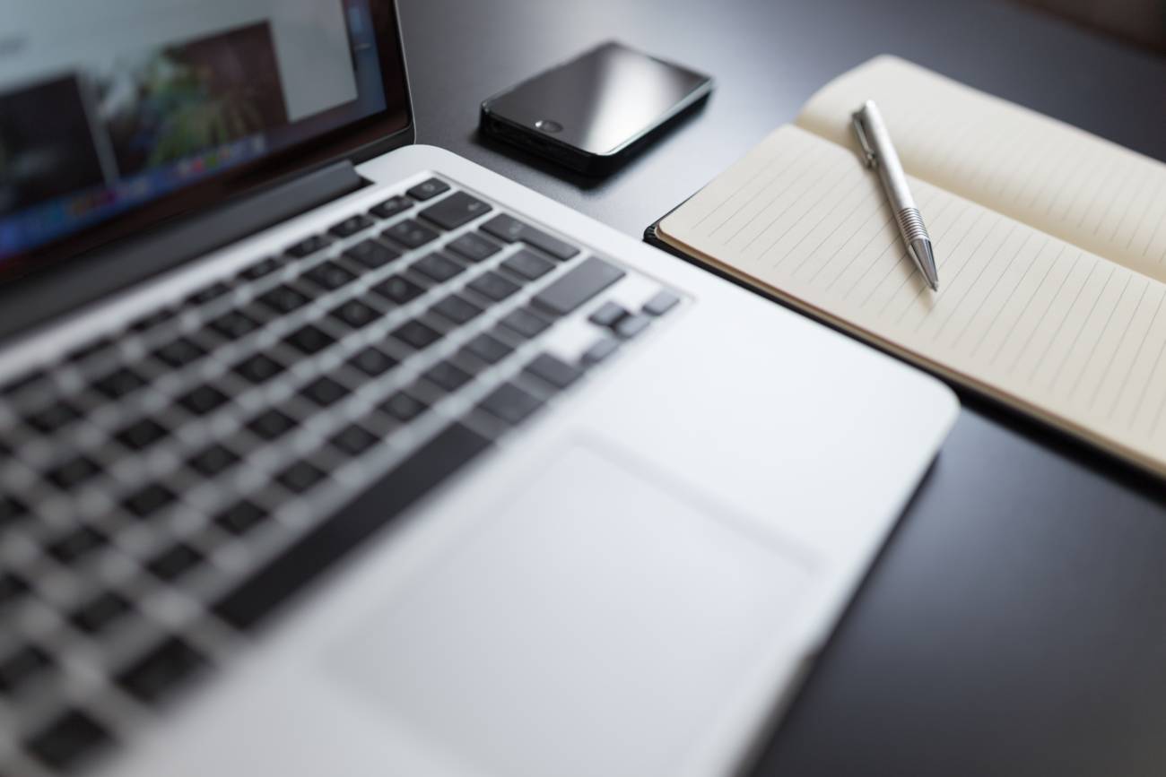 open laptop next to phone, paper and pen