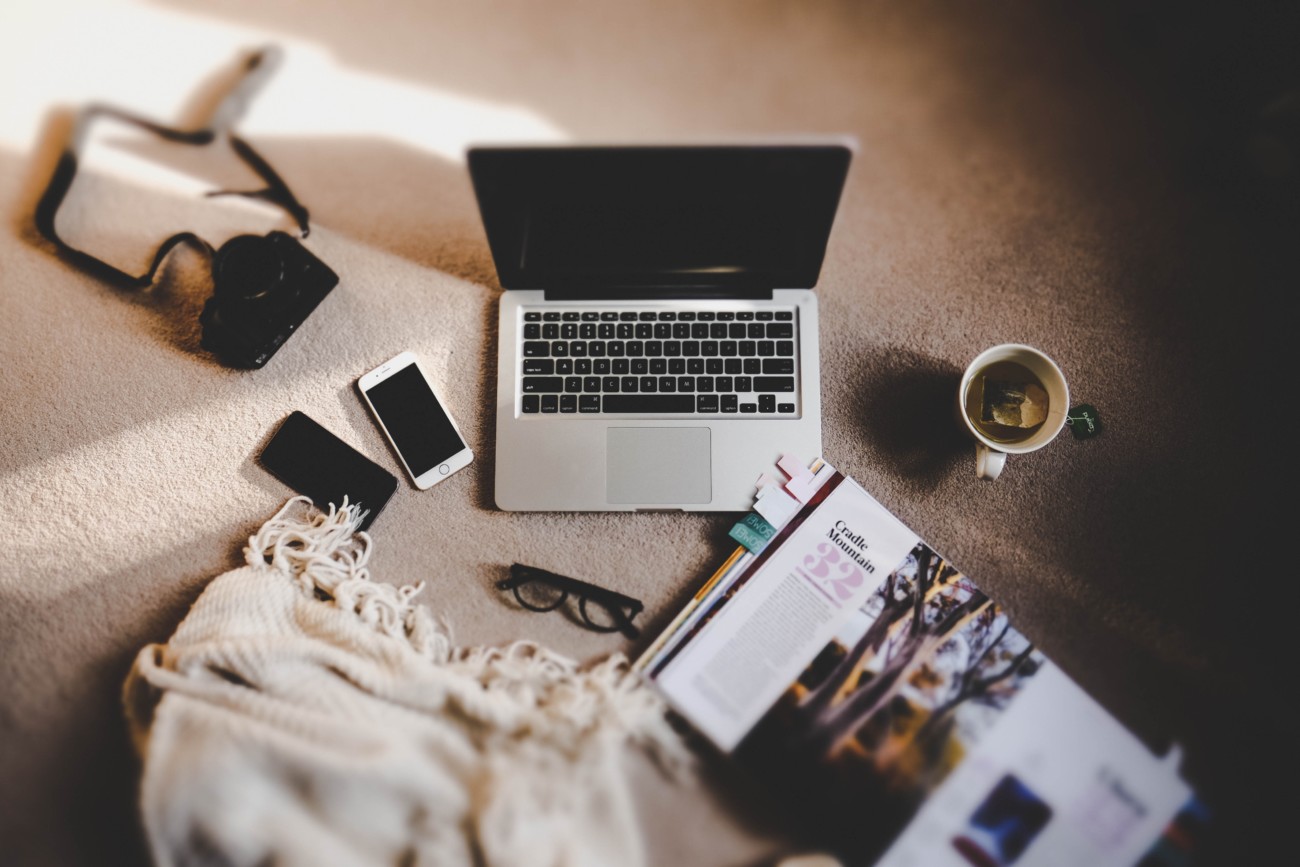 open laptop on floor next to phones, mug of coffee, blanket and open magazine