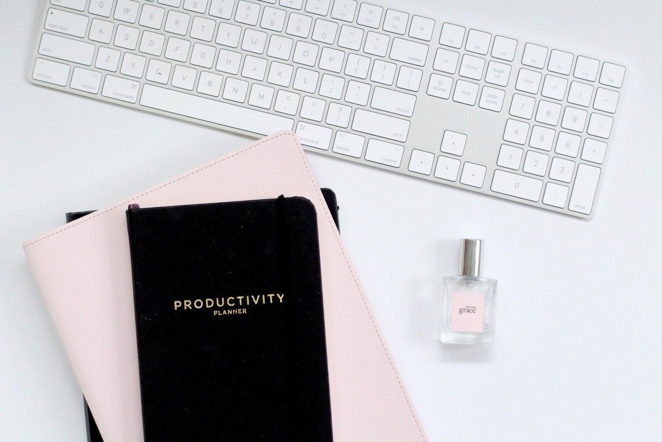 black notebook with the words 'productivity' on the front, on top of pink notebook next to computer keyboard