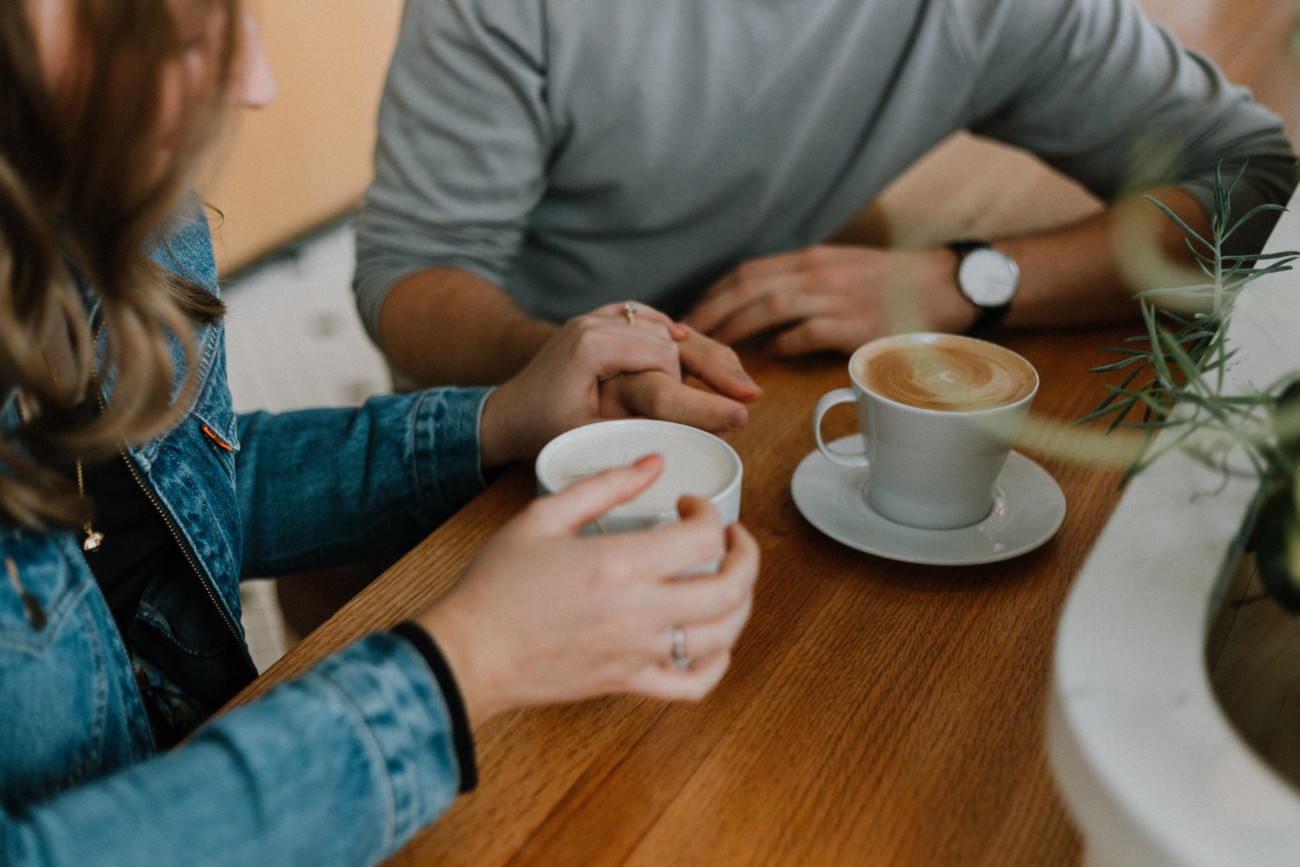 up close view of man and woman's hands holding mugs of coffee at table