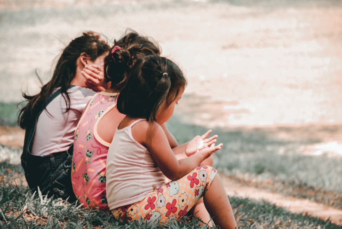 three young girls sitting together on grass