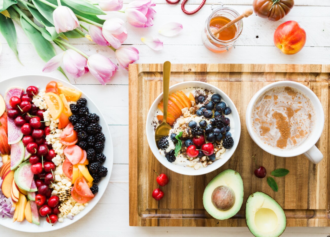 plates and bowls of fresh, healthy food with lots of fruit on a table and a wooden chopping board