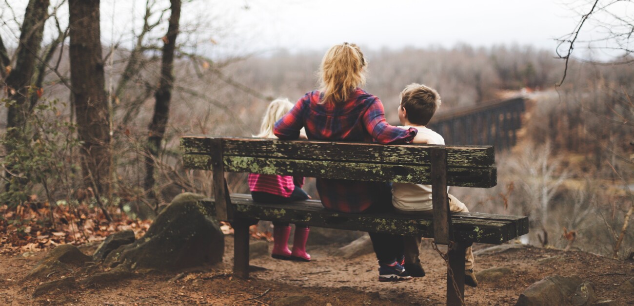 woman and boy and girl sitting on bench looking out at view