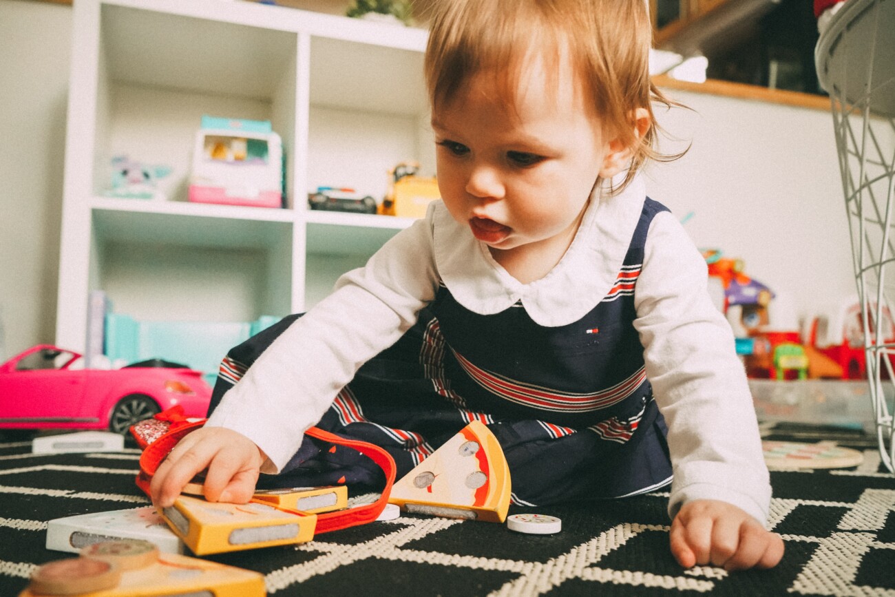 toddler girl playing on floor with toys in nursery