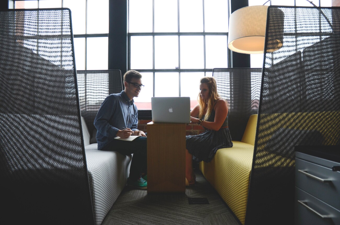 two people in a meeting sat in front of a window looking at a laptop on a table