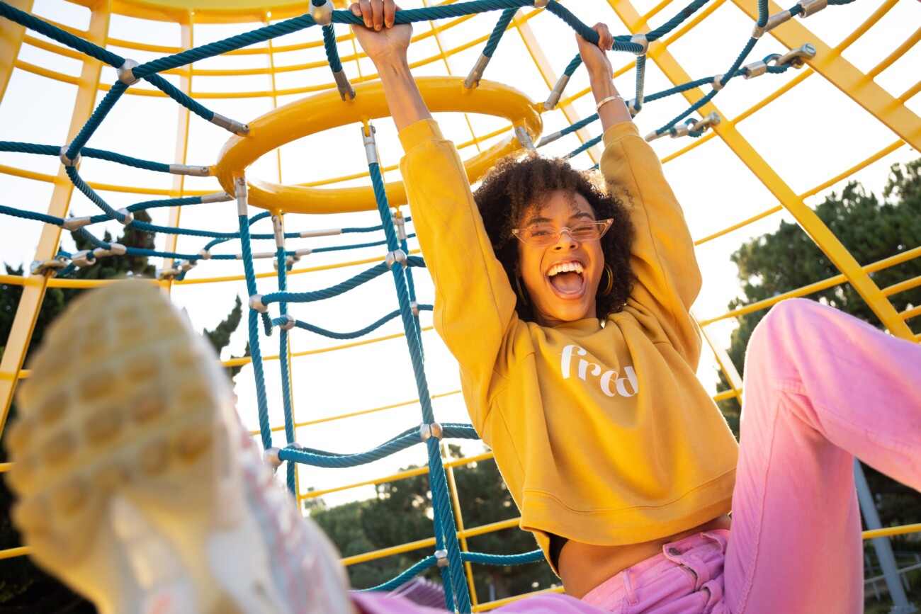 woman with a big smileon her face hanging on playground equipment