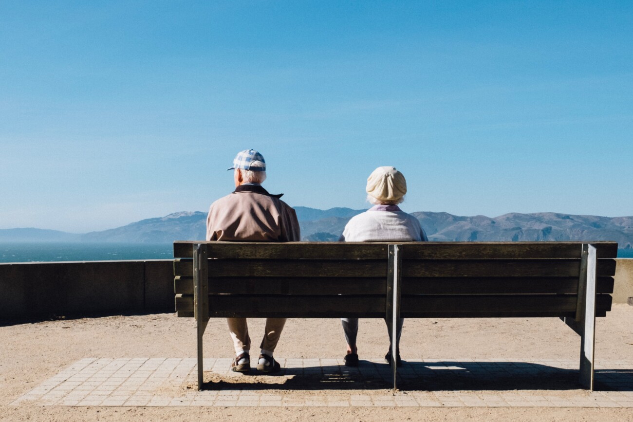 two old people sitting on a bench looking out of view