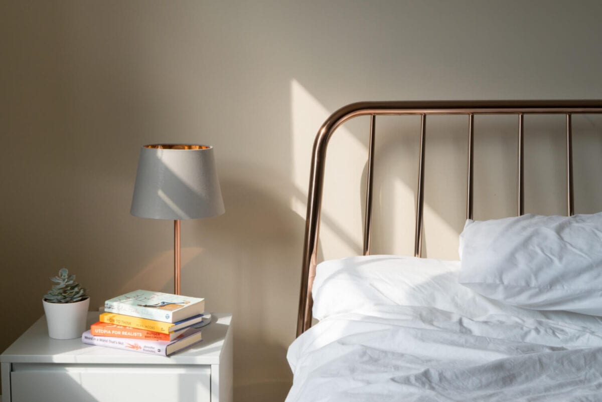 bed with white covers on it next to bedside table with books and lamp on
