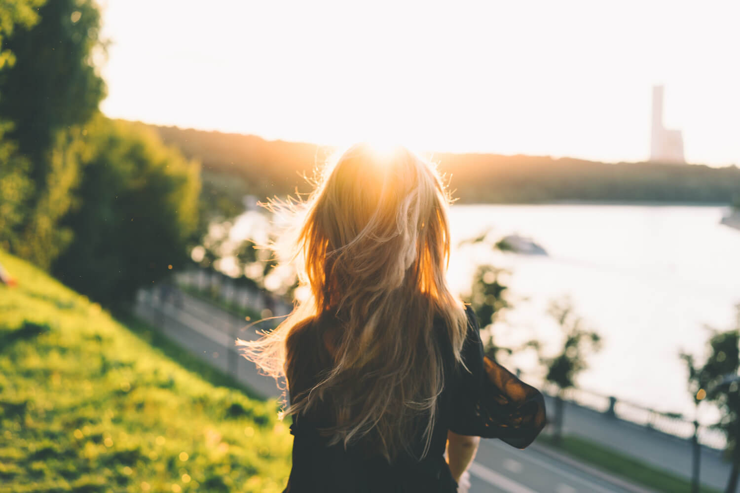 woman with long hair standing outside looking at view over water
