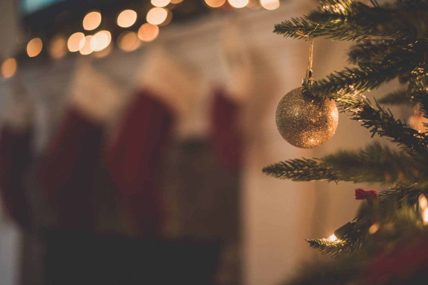christmas tree with gold baubles and stoclings hanging on the white fireplace behind