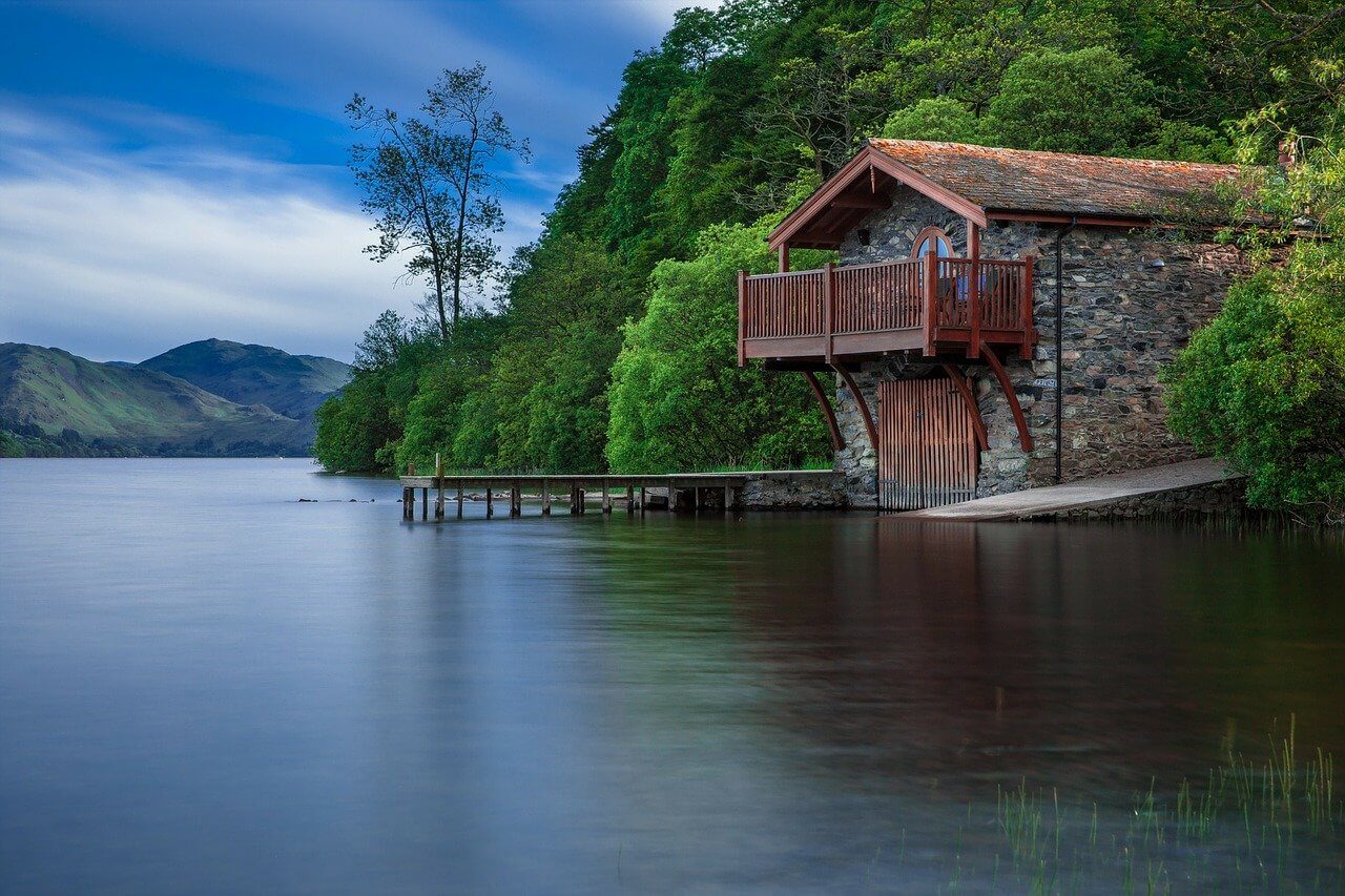 wooden lake house on the edge of the lake next to tree-covered mountains
