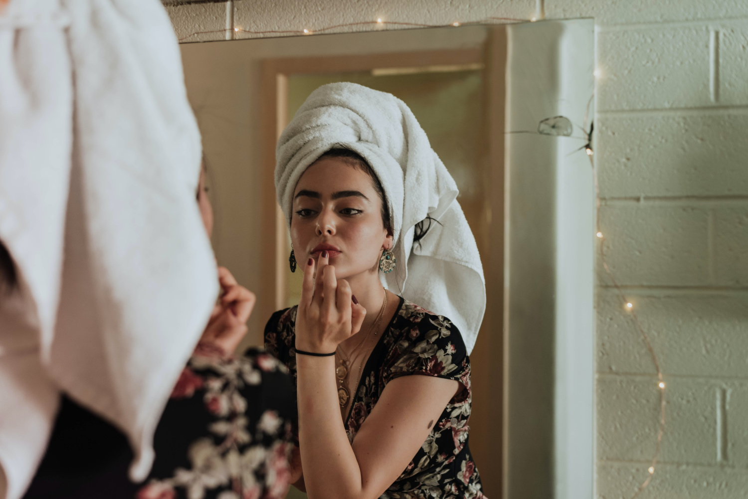 woman with a towel on her head looking into a mirror and putting something on her lips