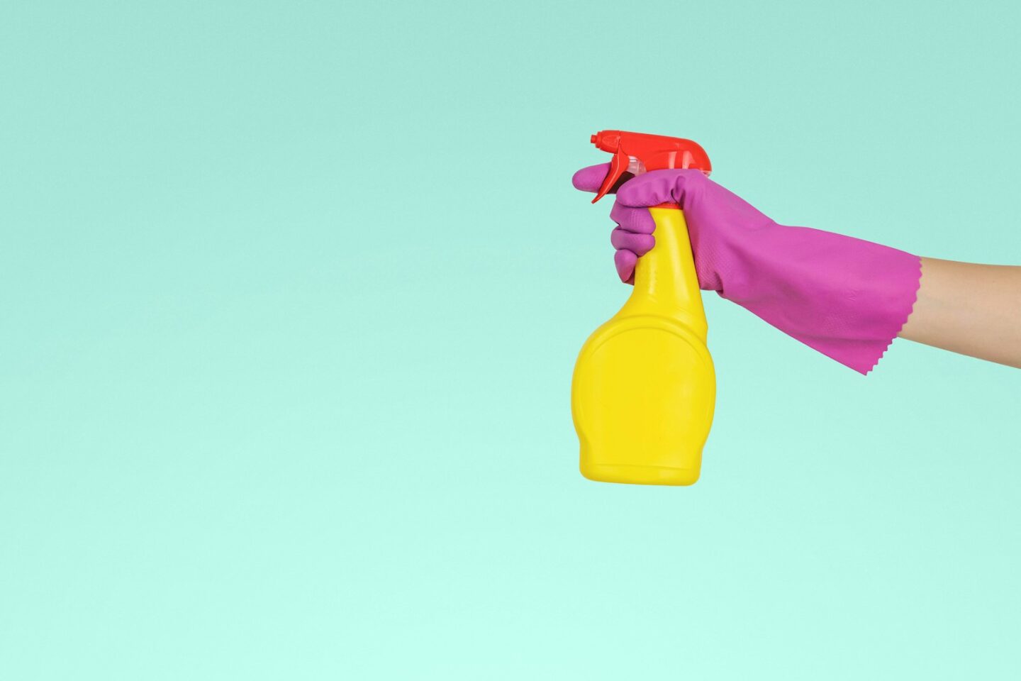 hand wearing bright pink rubber glove holding yellow plastic spray bottle