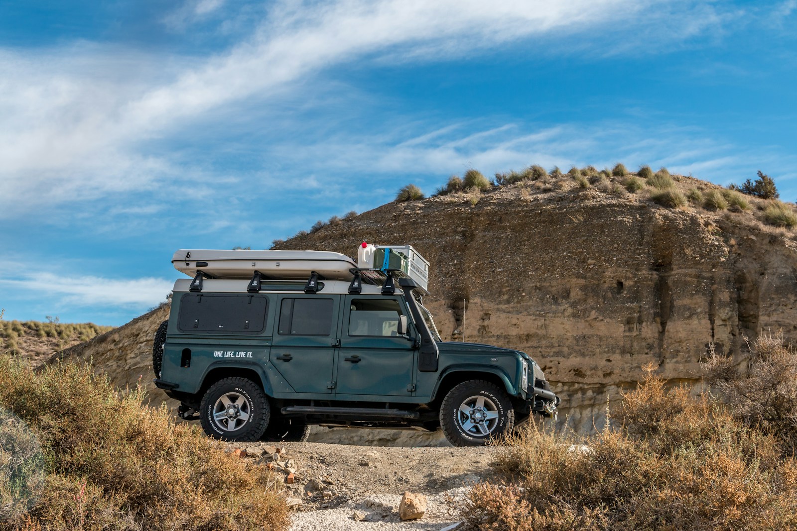 a jeep with a rooftop tent is parked on the side of a dirt road