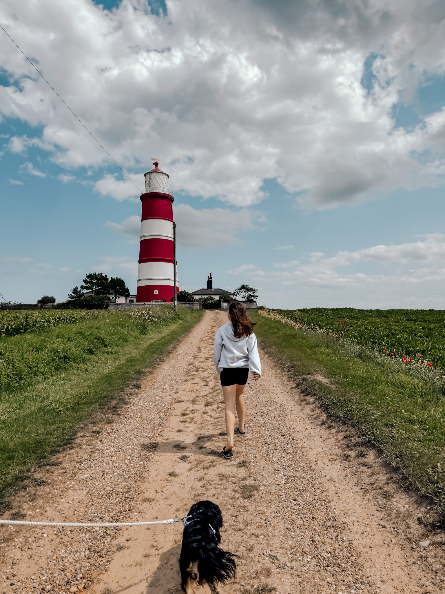 girl and black and tan cavalier dog walking up to Happisburgh Lighthouse in Norfolk