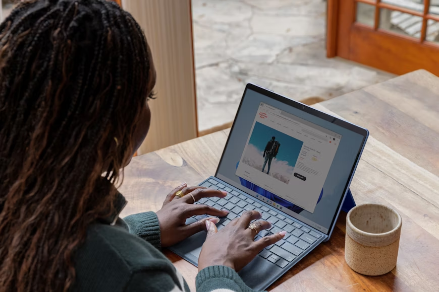 woman sitting at table typing at laptop with mug next to her