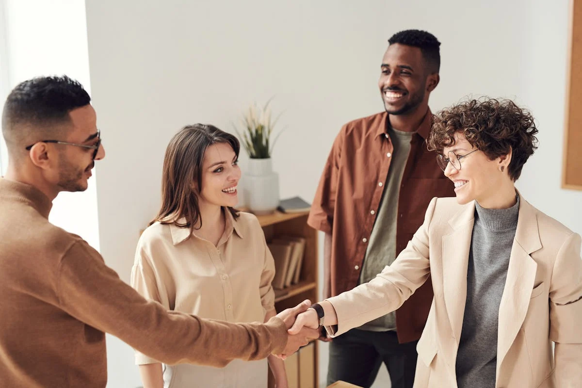 four people in a meeting shaking hands and smiling
