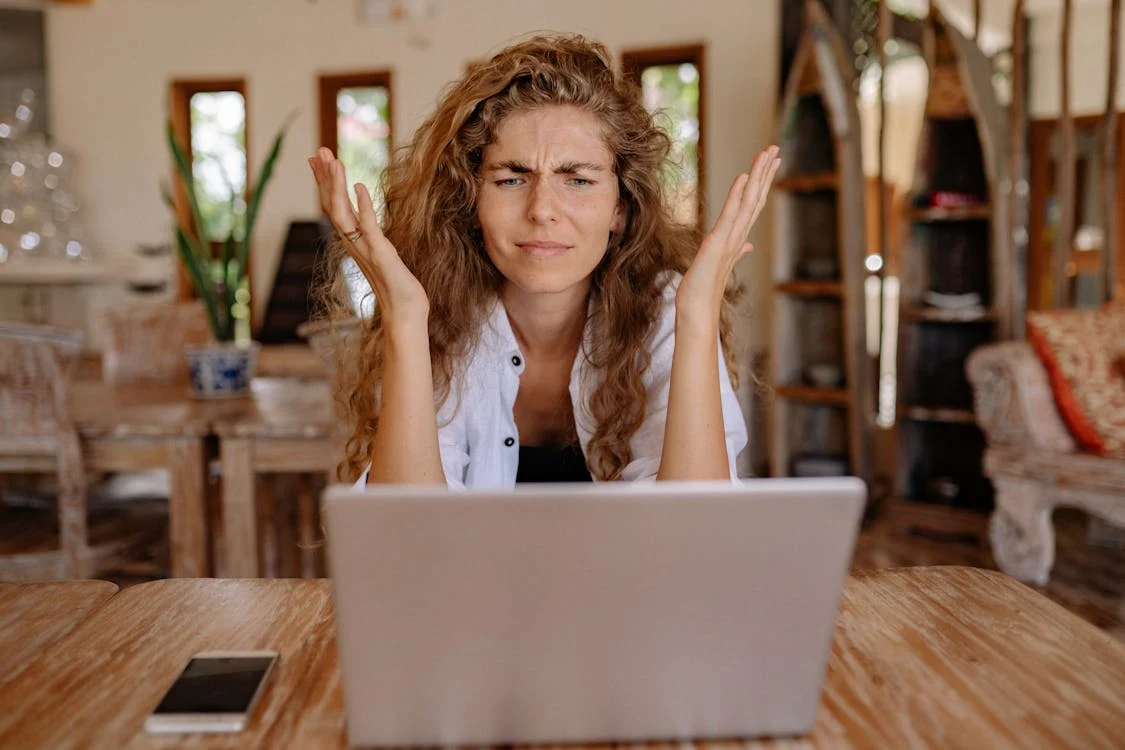 woman sitting at laptop on table with hands in the air in frustration