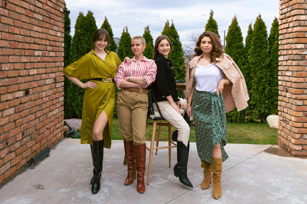 four women outside, in stylish outfits, posing for the camera