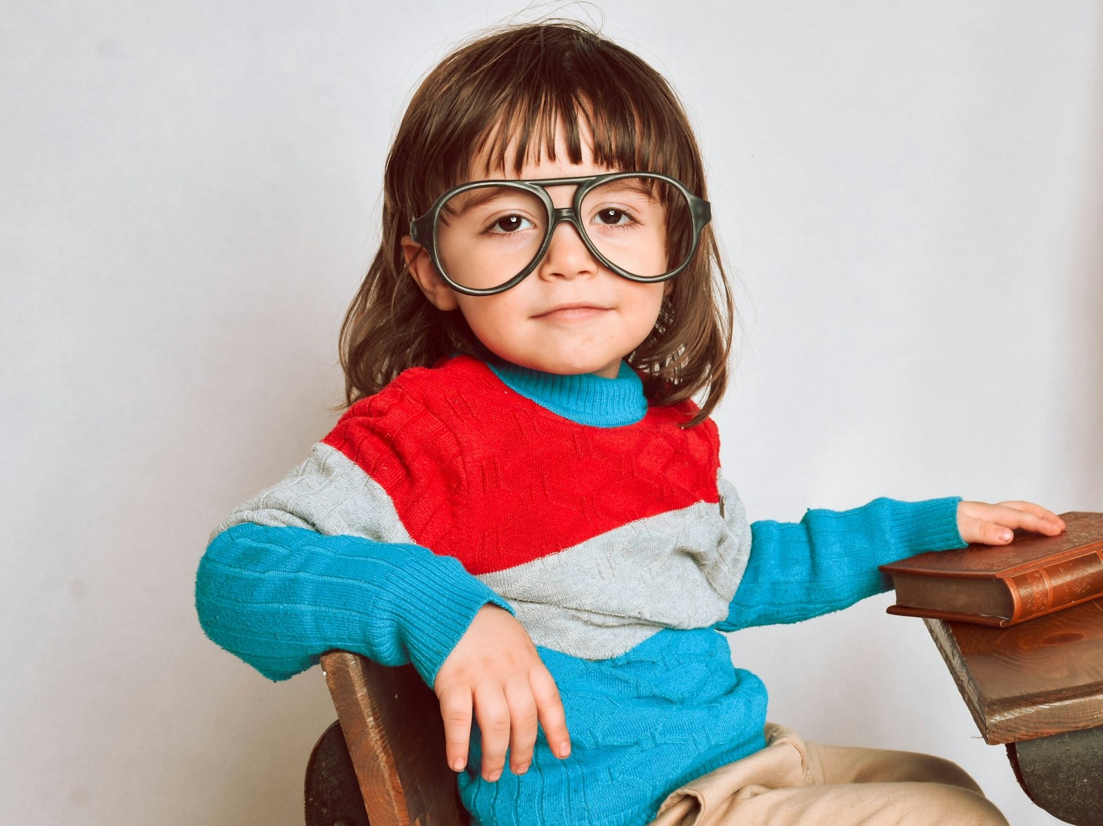 girl in big glasses and grey, blue and red sweater sitting on brown wooden chair