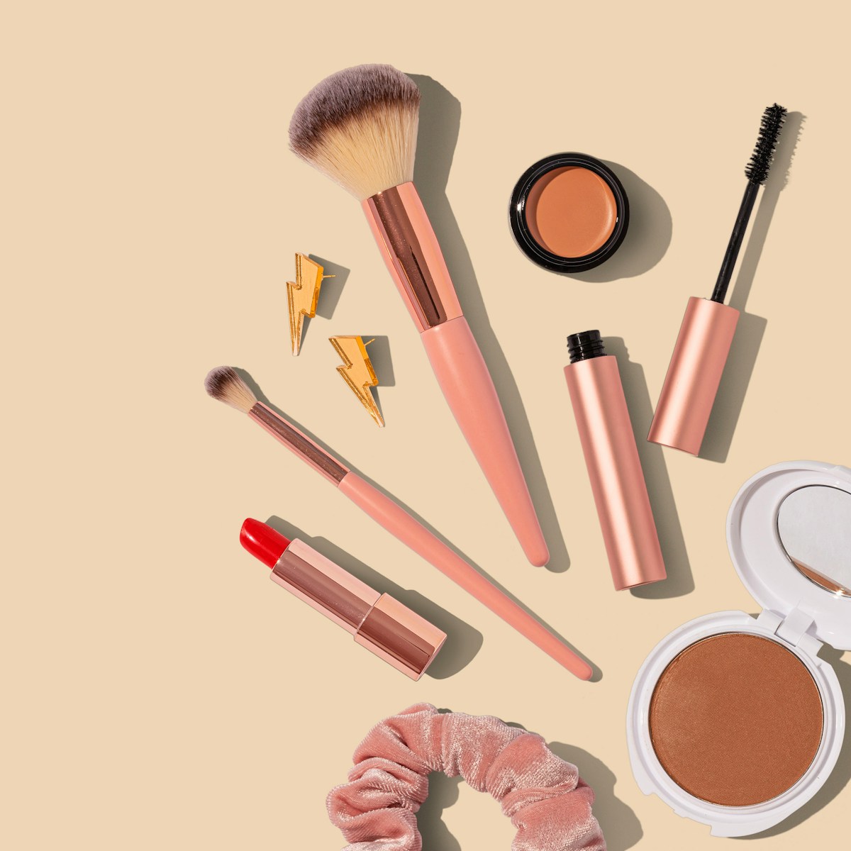 flatlay of makeup, brushes, scrunchie and lightening bolt earrings