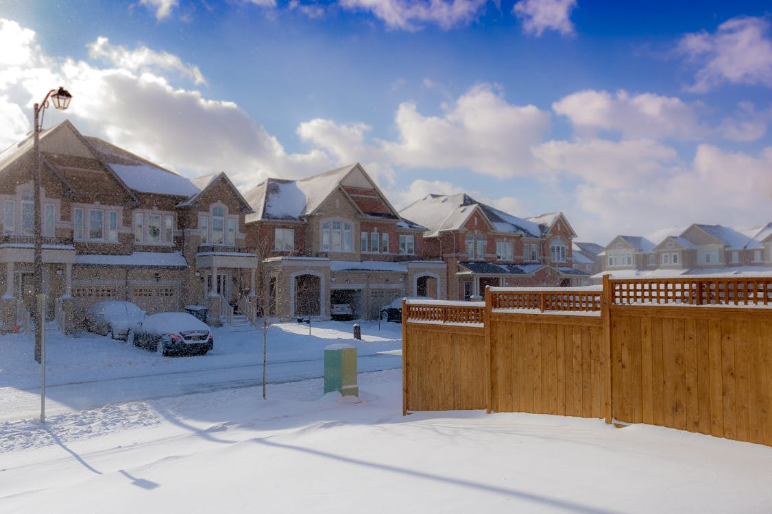 houses covered in snow and driveway next to fence