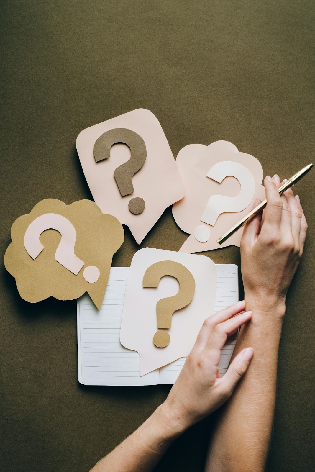 paper with cut-out question marks on and person's hand holding pen from above
