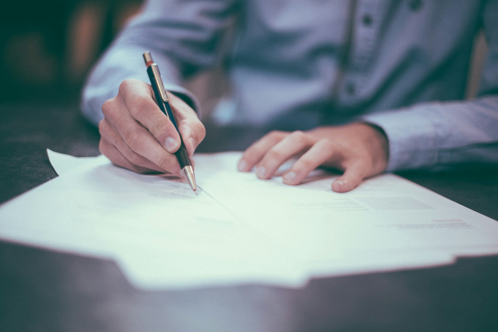 man in shirt writing on paper at desk