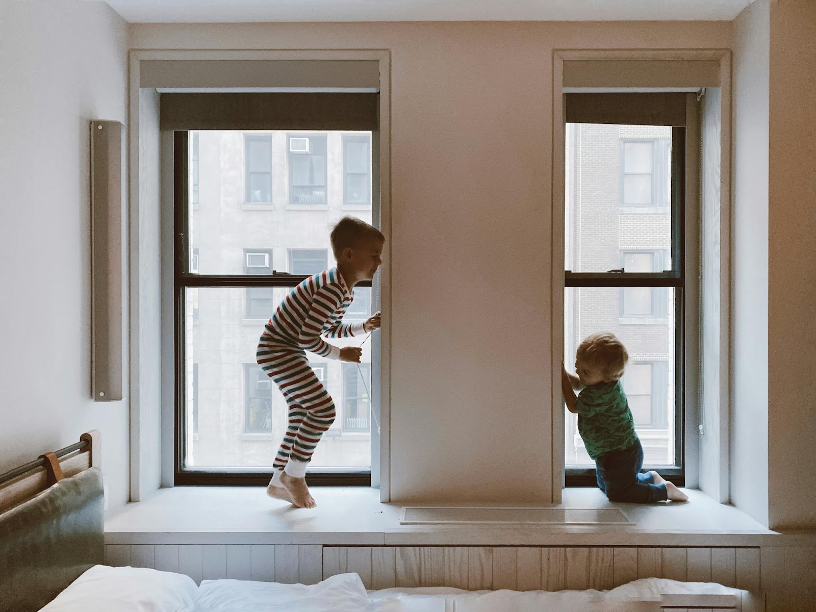 two young children standing and sitting in window at home