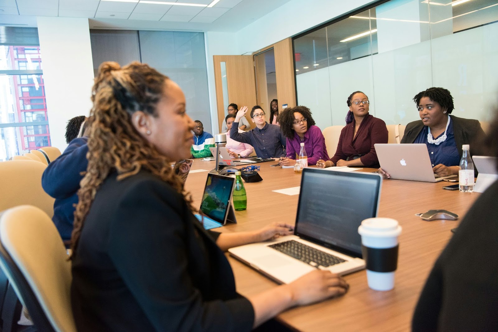 people in business meeting sitting with laptops at large desk with woman smiling, coffee cups on desk