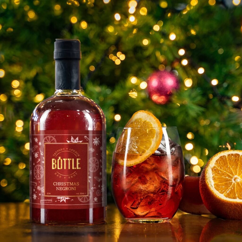 Negroni cocktail bottle with Christmas tree behind it