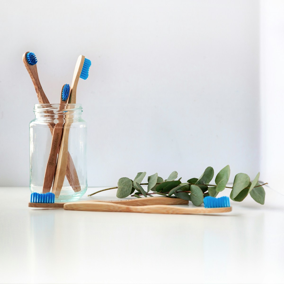 blue and white toothbrushes in clear glass jar with two more lying down next to it