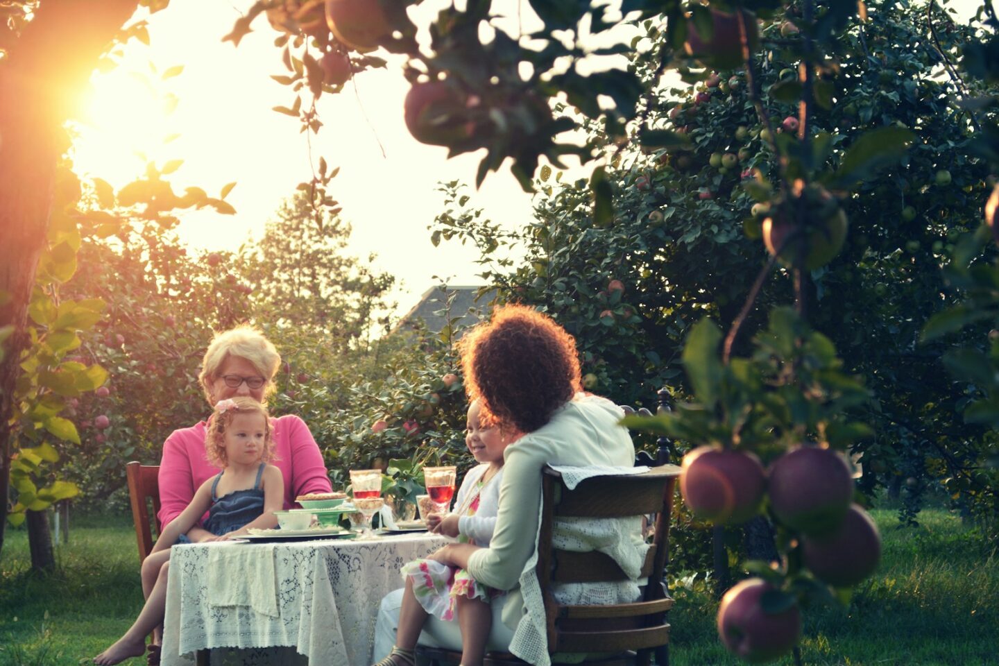 two women and carrying two children while sitting at table in garden with trees