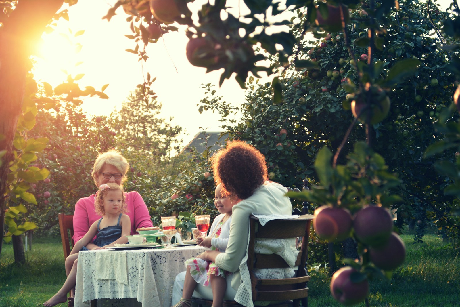 two women and two children sitting at table in garden with trees