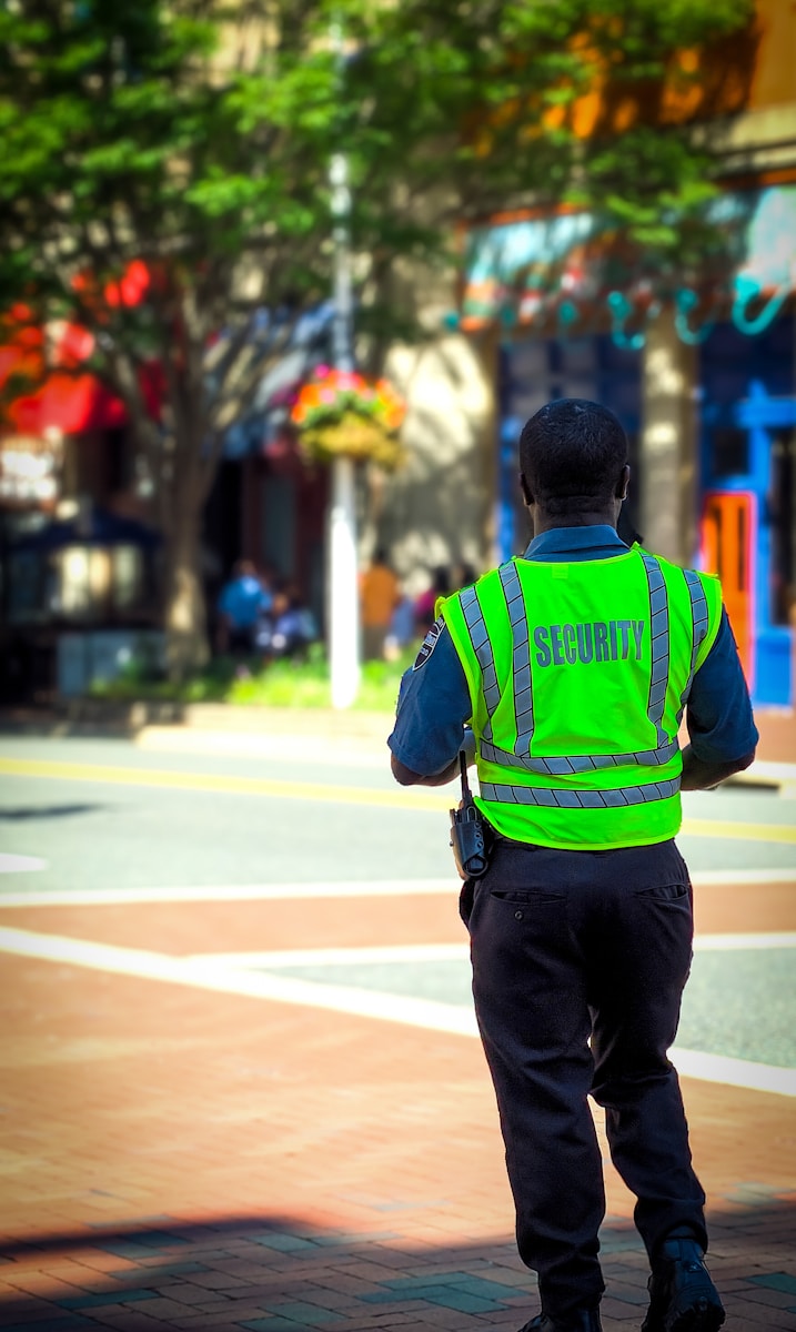 male security guard from the back, in green hi-vis vest on the street during daytime