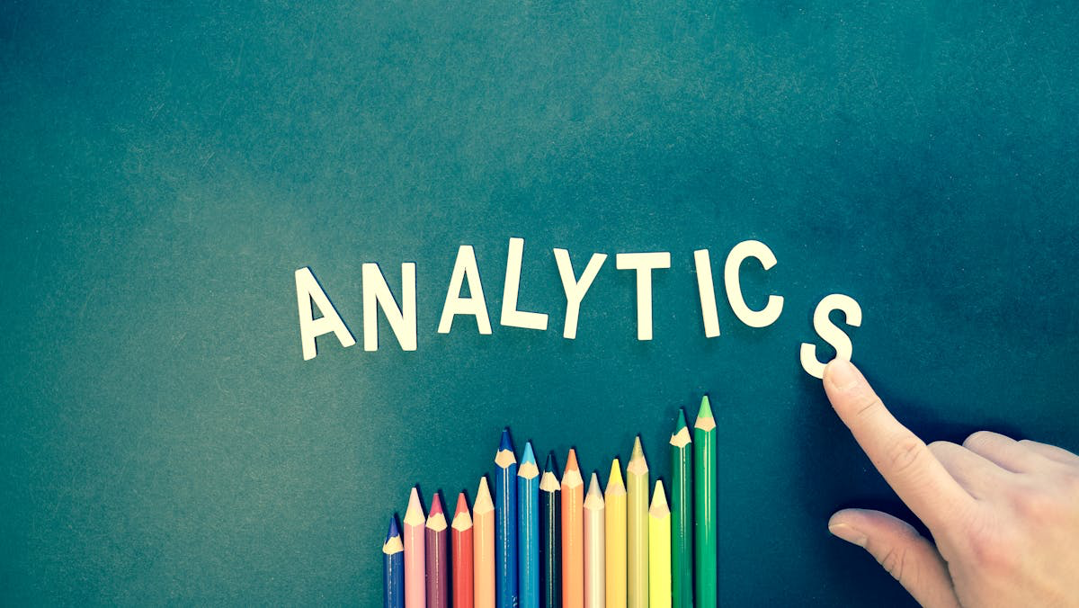 letters spelling out the word analytics with a finger pointing to the s which is falling down, an coloured pencil crayons below it