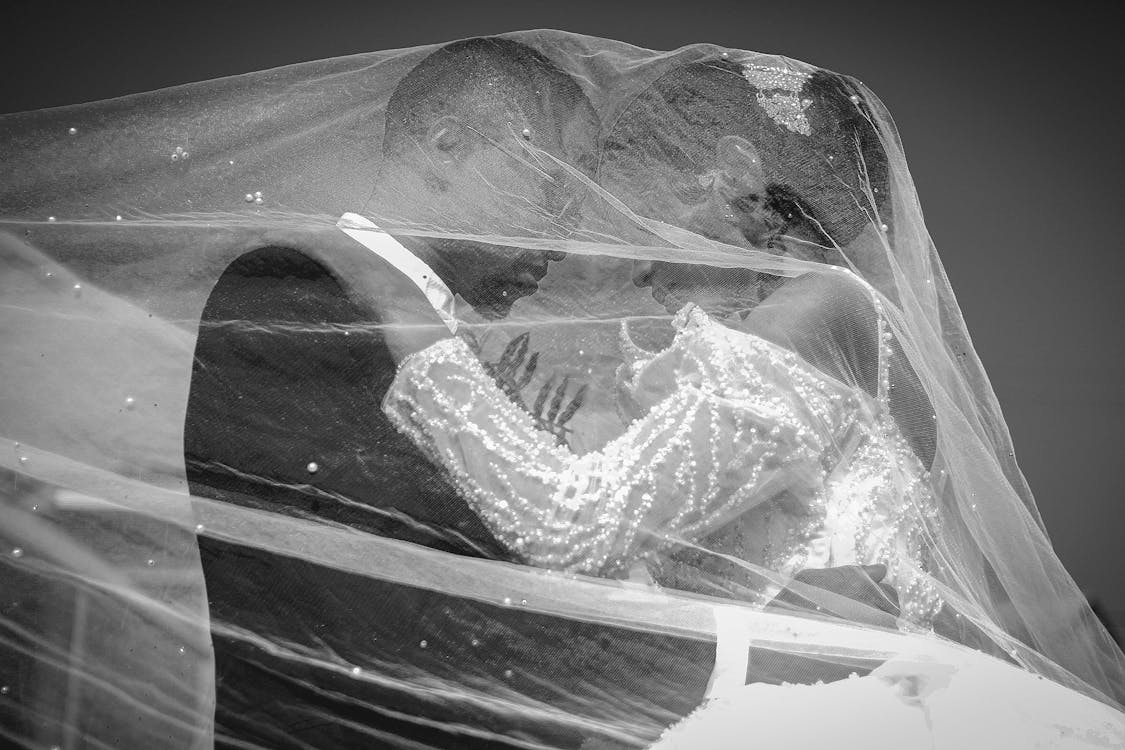 black and white photo of bride and groom under brides veil