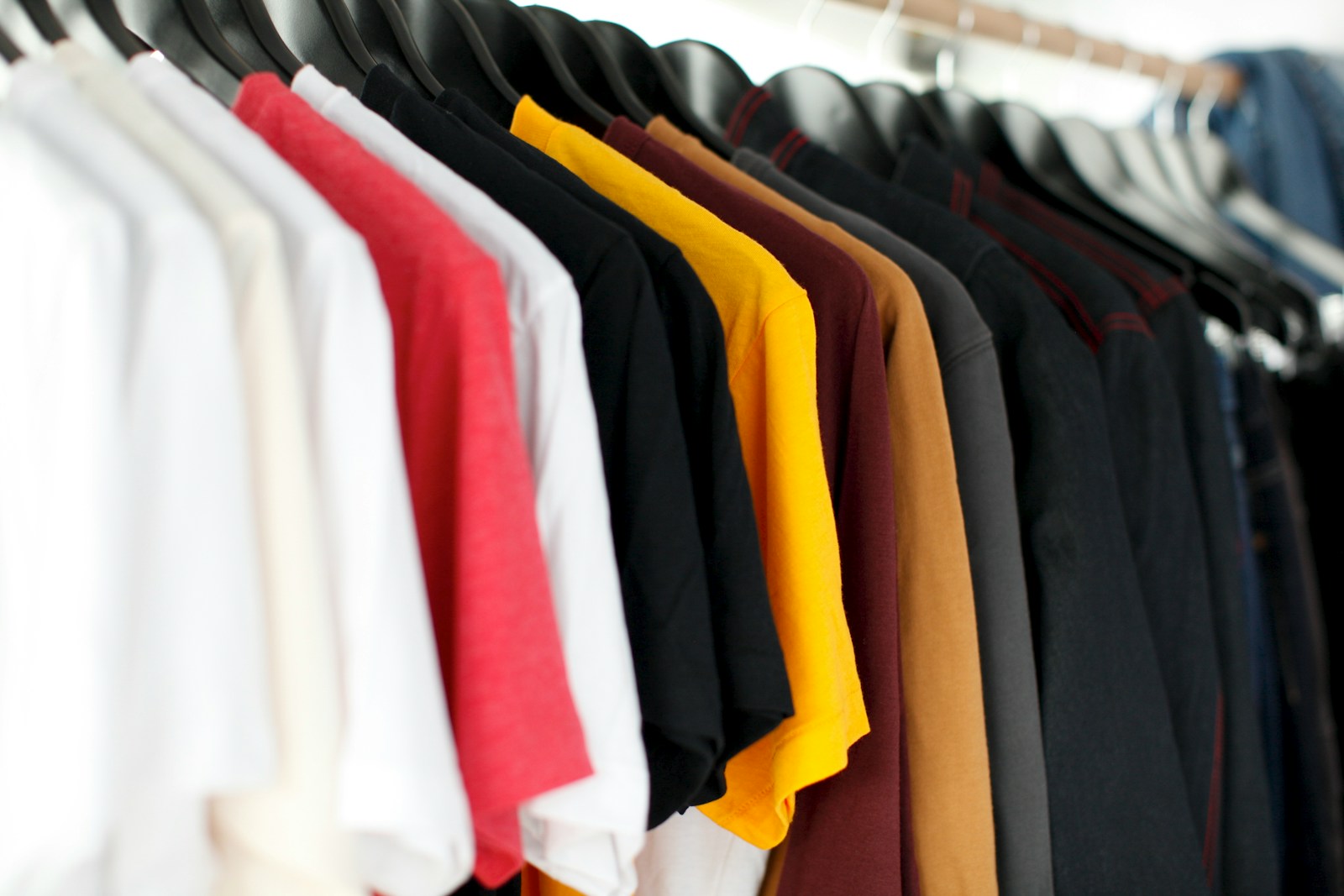 closeup of different coloured t-shirts hanging on rail