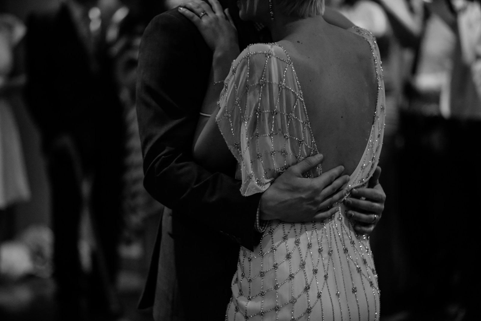 grayscale photo of woman wearing wedding dress with grooms arms around her for first dance