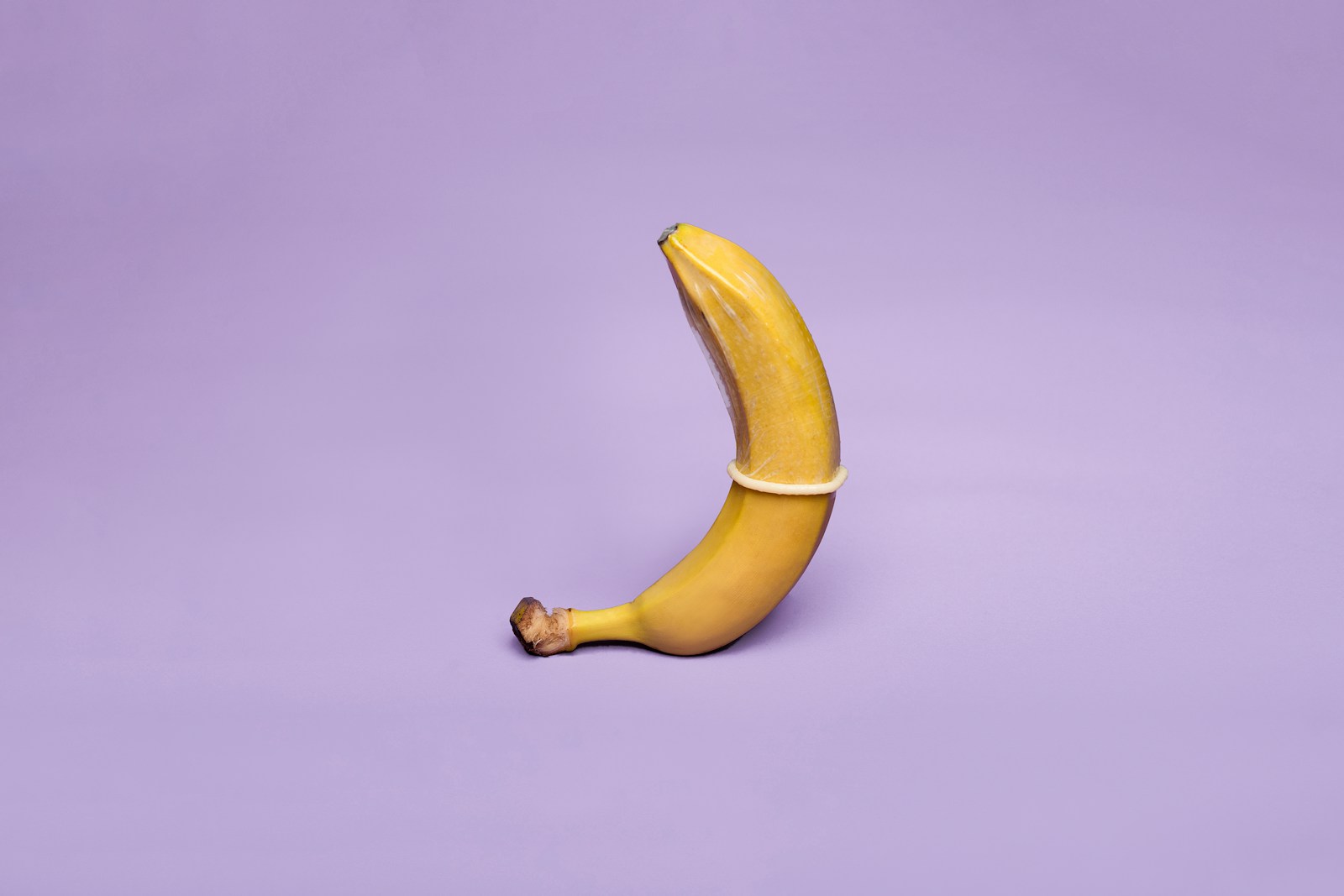 yellow banana with condom on on lilac table