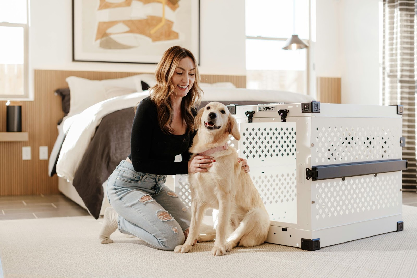 woman kneeling on bedroom floor with hands on dog sitting next to white plastic dog crate