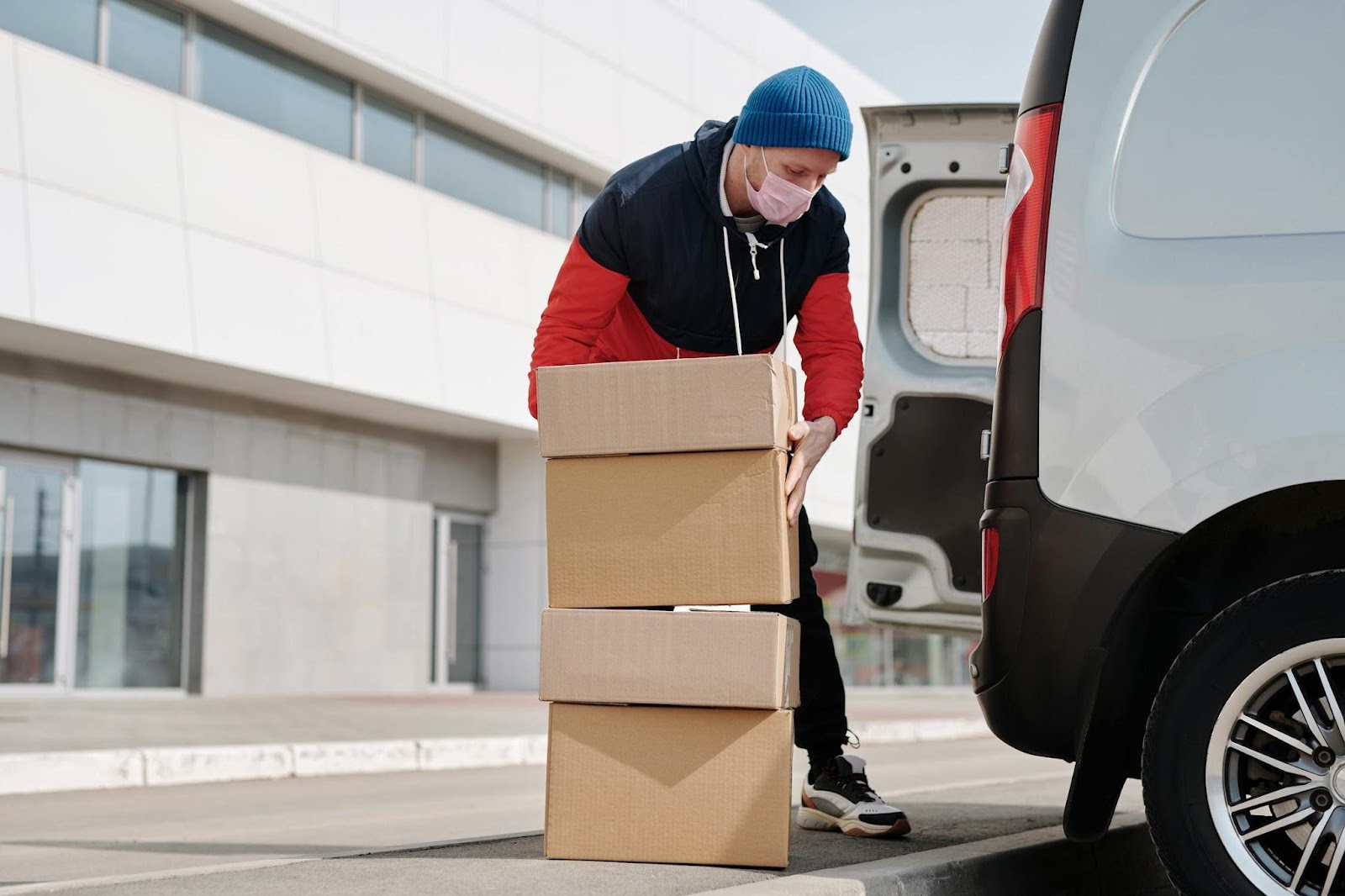 man in blue woolly hat and face mask bending down to pick up boxes to load in white vam